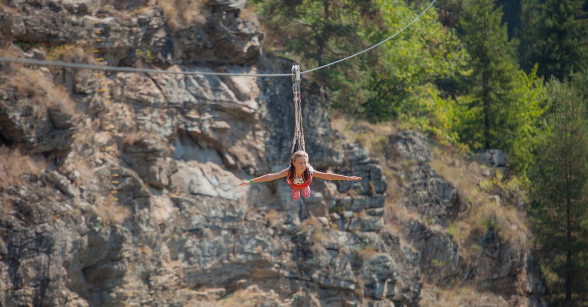 A young girl enjoying a thrilling zipline ride through a scenic rocky canyon outdoors.