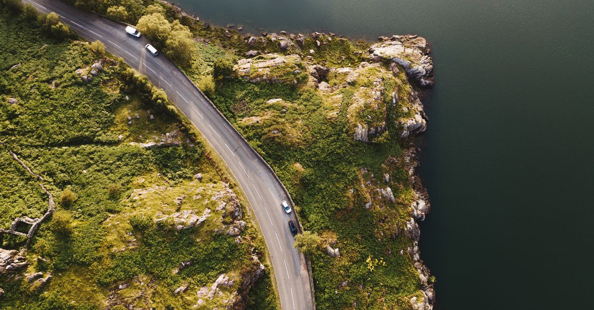 A stunning aerial shot of a winding road along a rocky coastline surrounded by lush greenery.