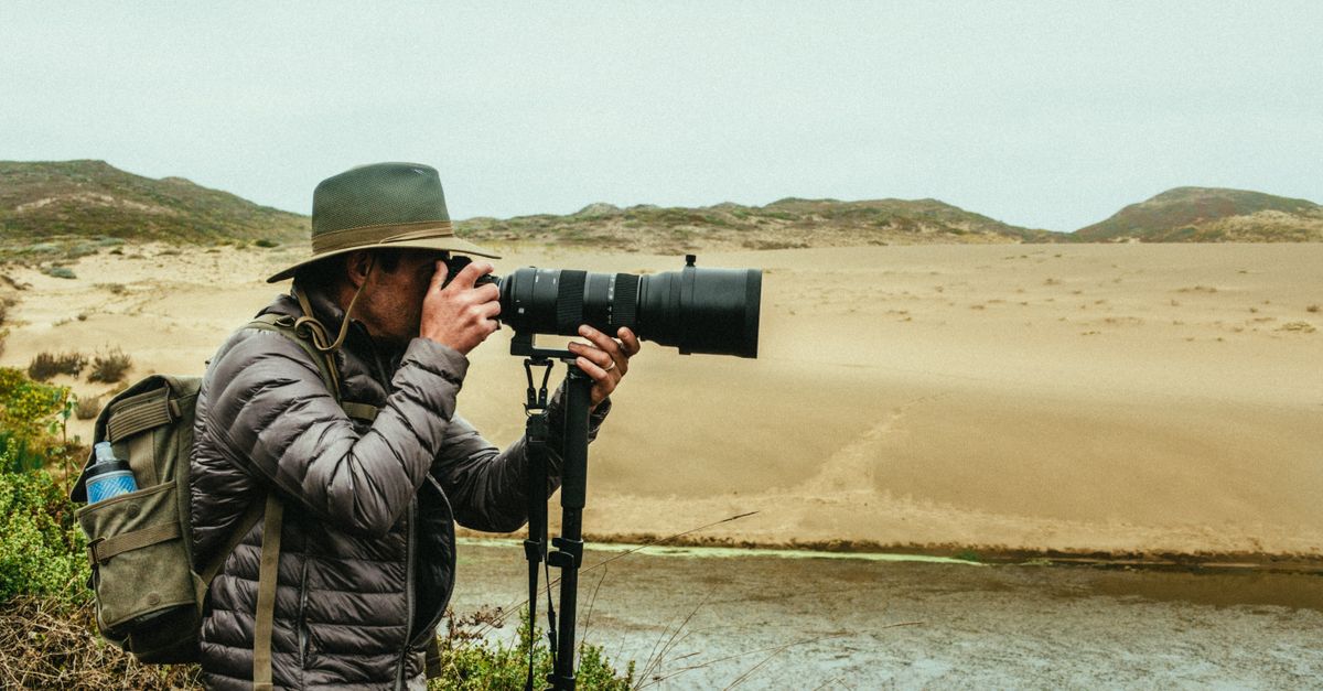 Man photographing desert scenery with camera and tripod outdoors.