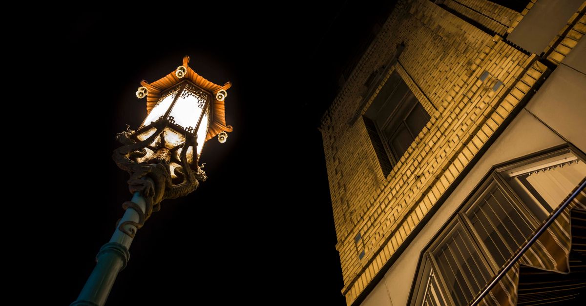 Illuminated Chinatown lamp post beside a historic building in San Francisco at night.