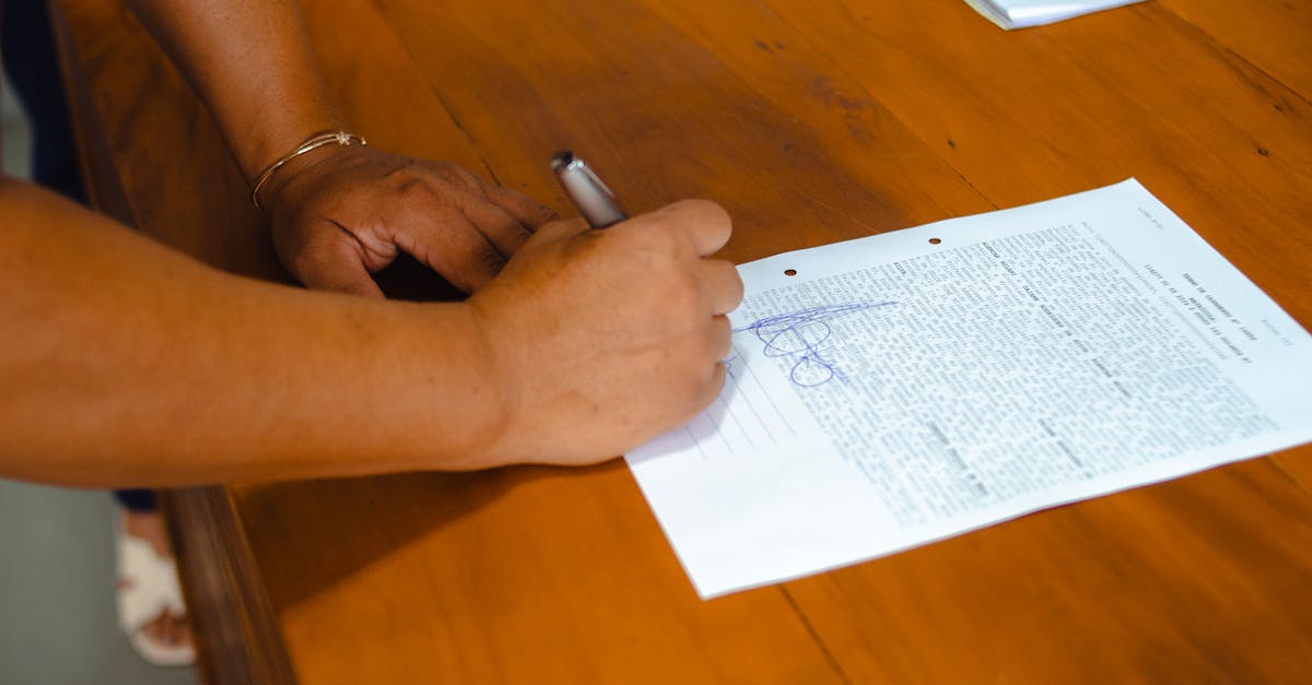 Close-up of hands signing a legal document on a wooden table indoors.