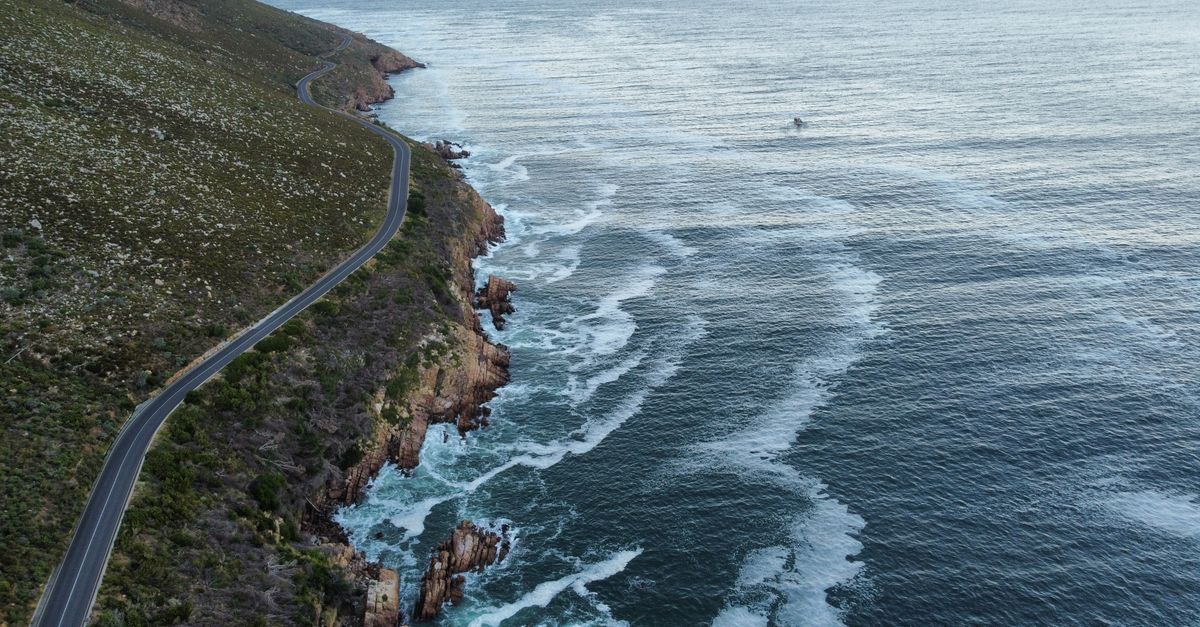 Aerial view of a winding coastal road along a rocky shoreline with ocean waves.