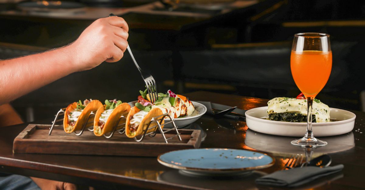 A flavorful dining setup featuring tacos, a refreshing beverage, and a gourmet plated dish indoors.