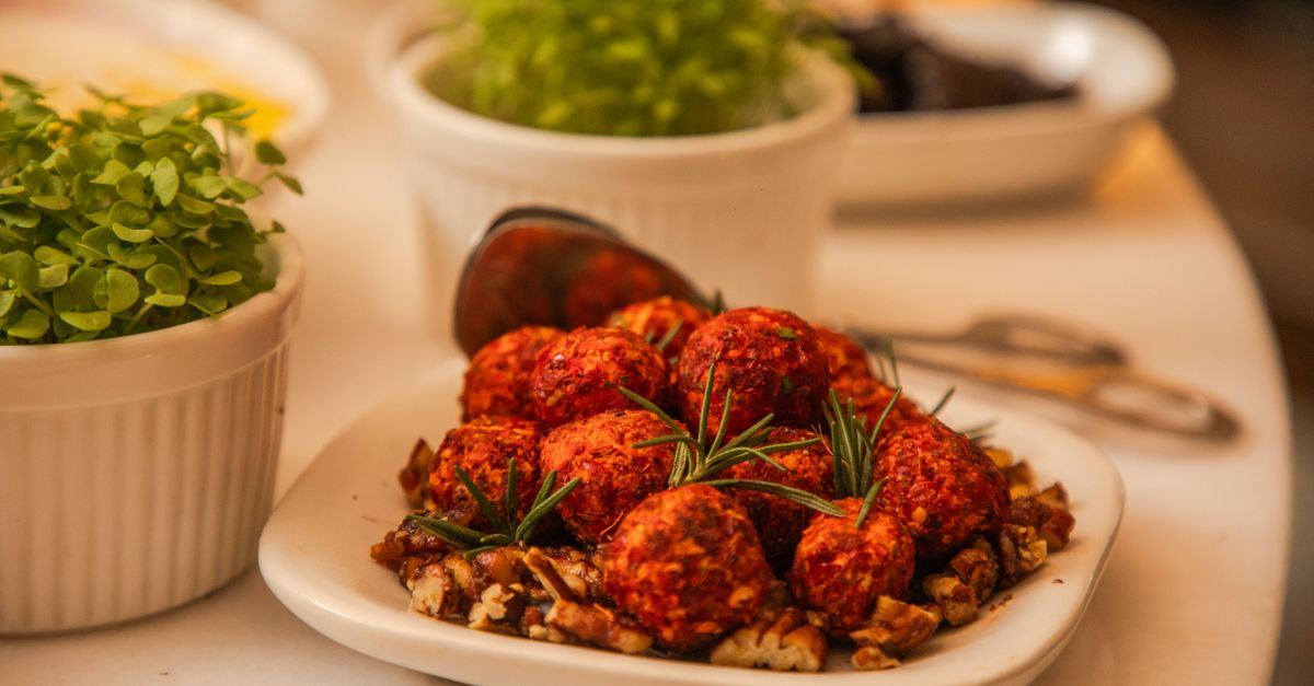 Close-up of spicy cheese balls garnished with rosemary and nuts, surrounded by fresh herbs.