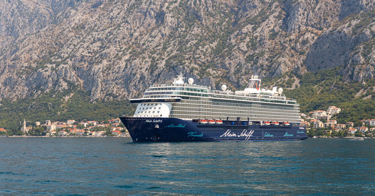 A luxury cruise ship sails against stunning coastal mountains and a serene seaside village.