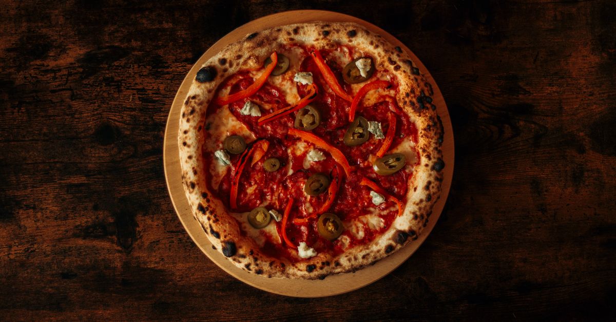 A gourmet pizza topped with red peppers and olives on a rustic wooden table. Perfect for food lovers.