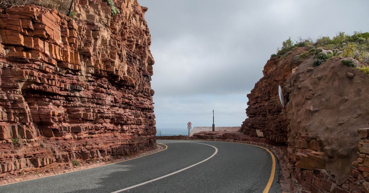 Winding road through red sandstone cliffs in Cape Town, showcasing natural beauty and adventure.