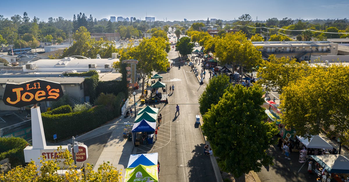 Aerial shot of a lively street market under blue skies in Sacramento with vendor tents and people.