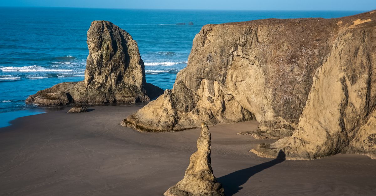 Stunning coastal rock formations at a sandy beach under clear blue skies.