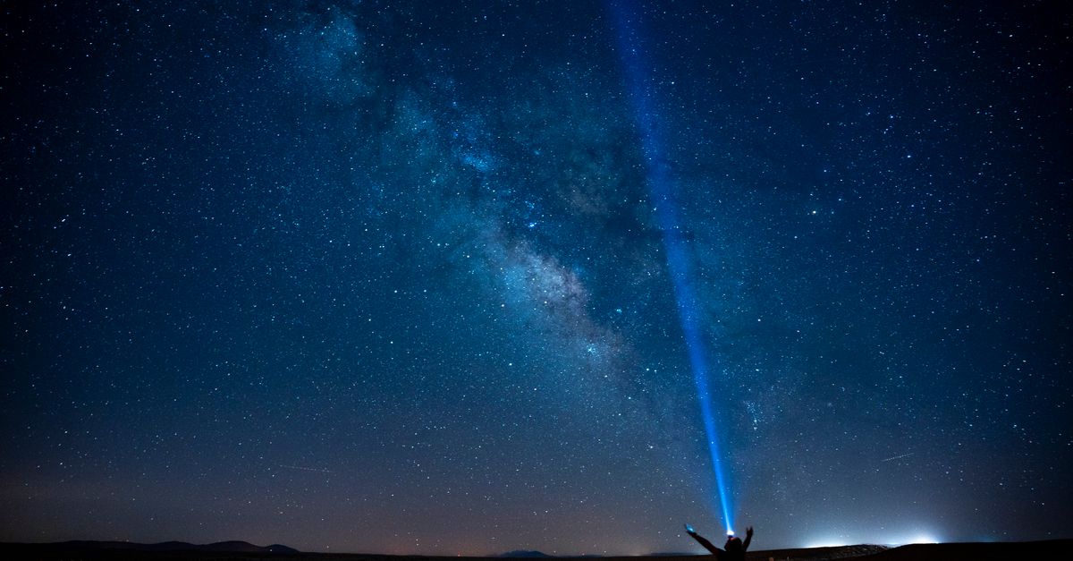 A person stands on a road under the Milky Way, pointing a beam of light into the starry night sky in Karaman, Türkiye.