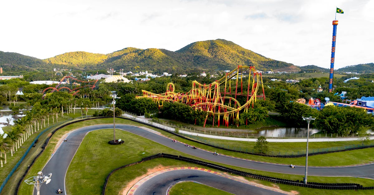 Aerial view of an amusement park featuring a roller coaster and go-kart track, set against a mountain backdrop.