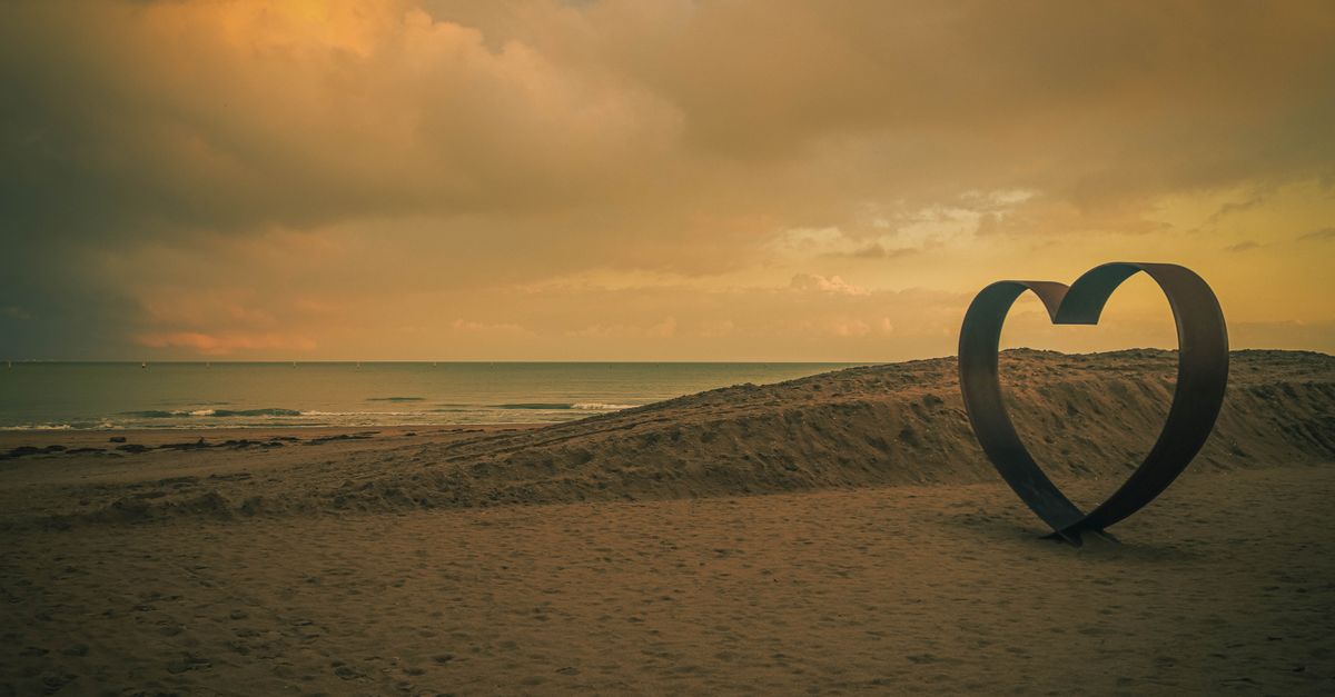 A heart-shaped sculpture on a peaceful beach at sunset, creating a romantic and serene atmosphere.