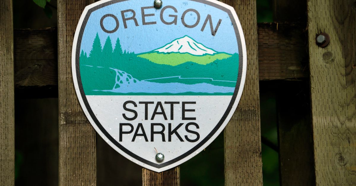 Oregon State Parks emblem sign mounted on a rustic wooden fence, surrounded by nature.