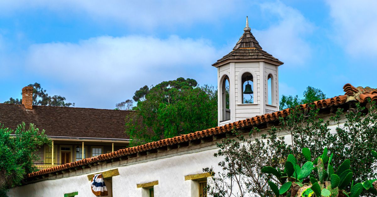 A picturesque view of a historic mission bell tower surrounded by lush greenery in San Diego, CA.