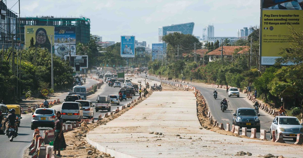 Traffic flows on a busy urban road in an African city with various vehicles and advertisements under a clear sky.