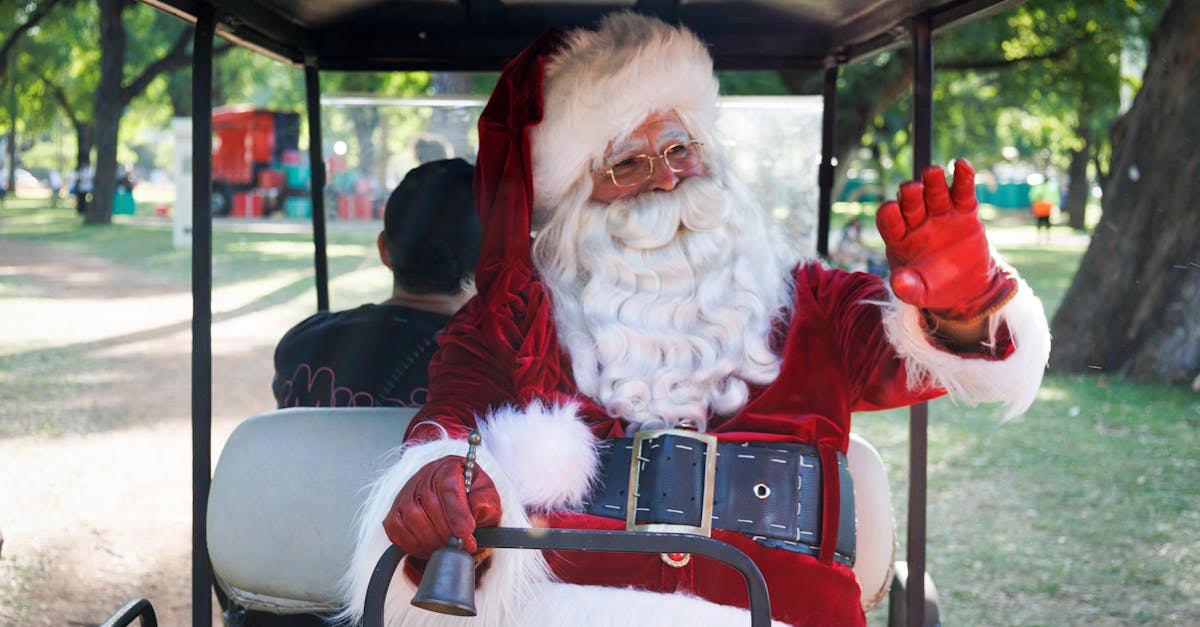 Santa Claus in a golf cart, waving with a bell in hand in a sunny park setting.
