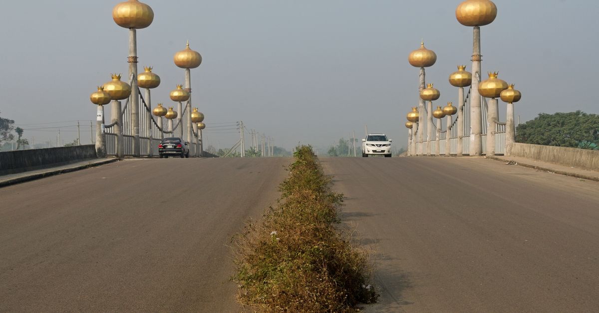 A scenic view of a bridge with golden dome pillars in Dhaka, Bangladesh under clear skies.