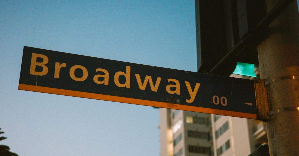 A vibrant street sign depicting Broadway during twilight with a city backdrop.