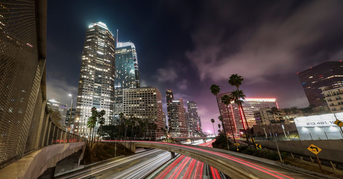 Dynamic night cityscape of Los Angeles with light trails, skyscrapers, and palm trees.