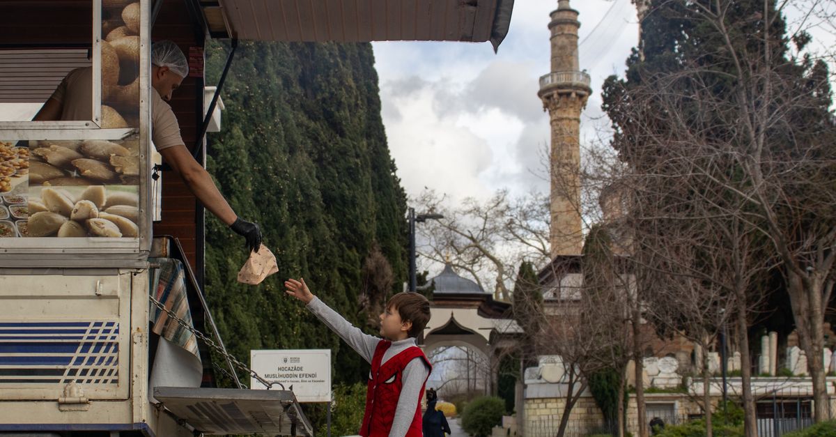 A young boy receives food from a street vendor near a mosque in a park.