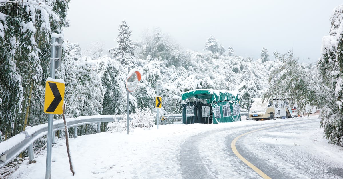 Scenic snowy mountain road with traffic signs and a tent under heavy snow. Ideal winter travel setting.