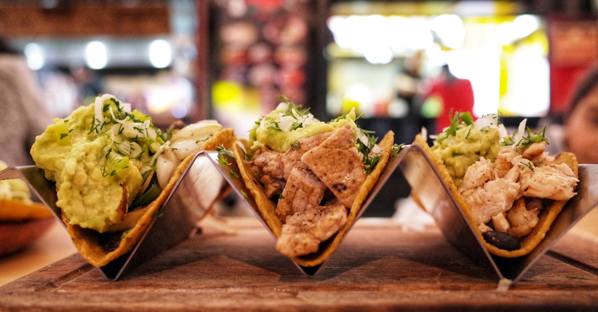 Close-up of three chicken tacos with guacamole, herbs, and onions in a restaurant setting.