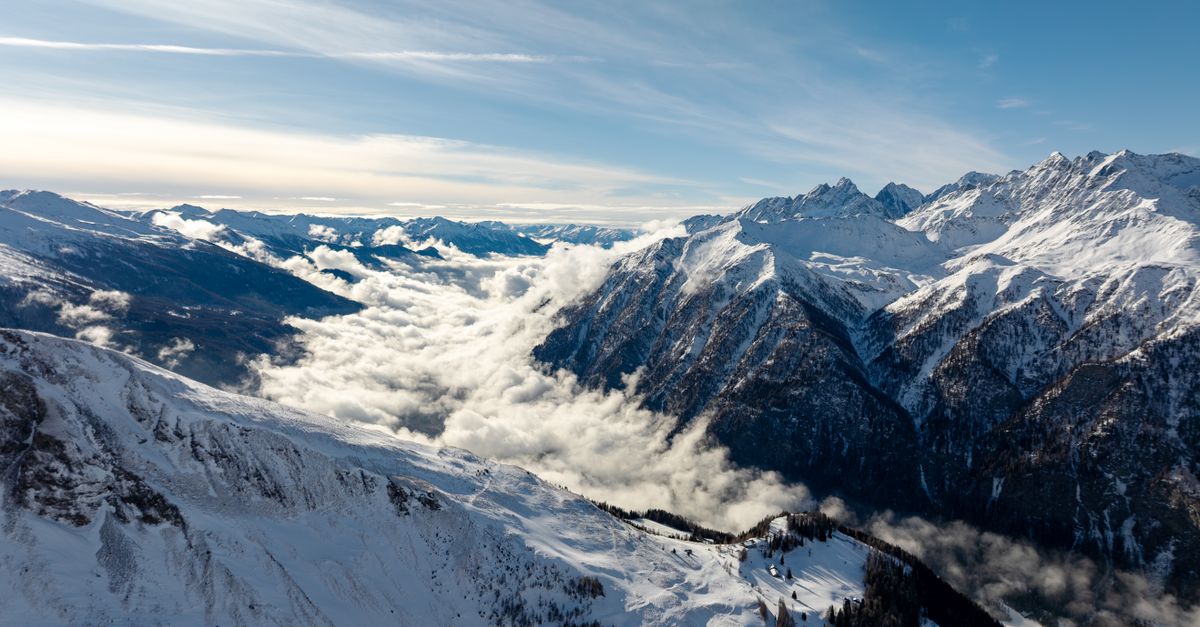 Breathtaking aerial view of snow-capped mountains in Korutany, Austria, with clouds nestled in valleys.
