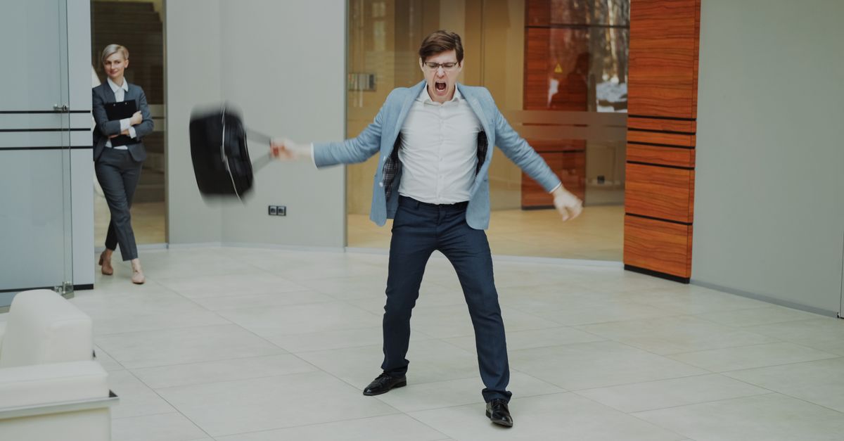 A businessman expresses frustration by throwing his briefcase inside a modern office setting.