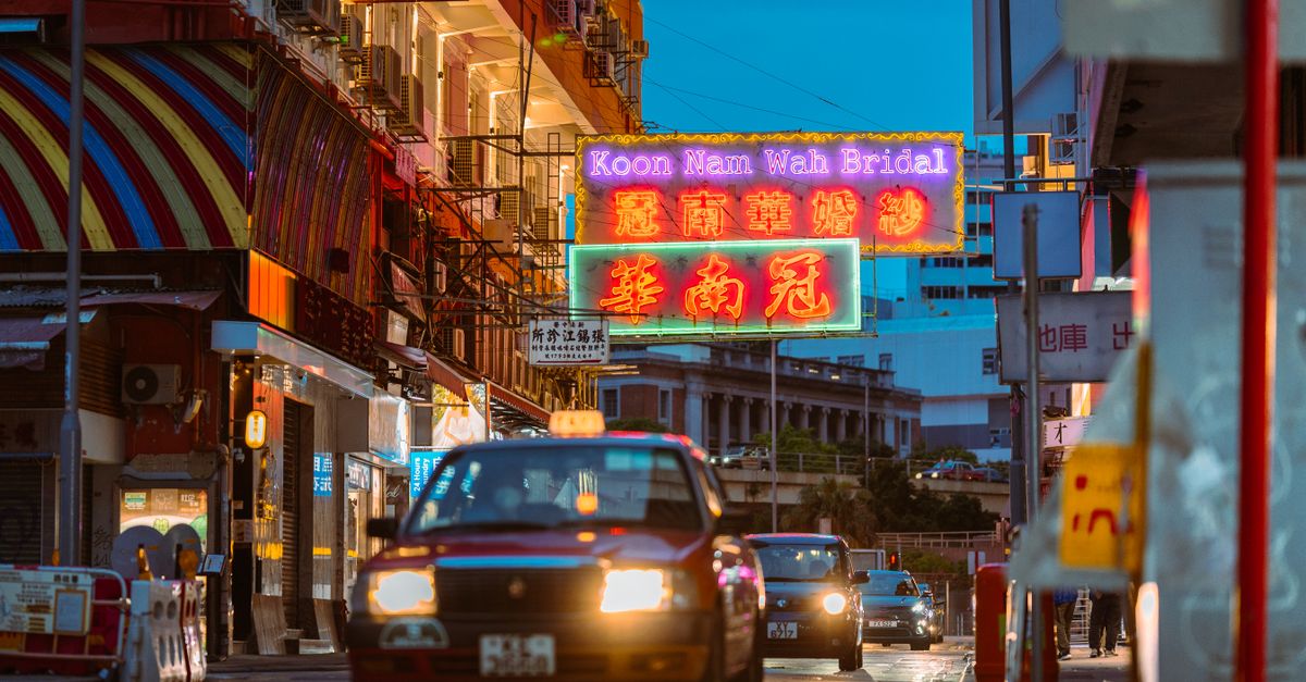 Neon-lit street with bustling traffic and vibrant signs in urban Hong Kong at twilight.