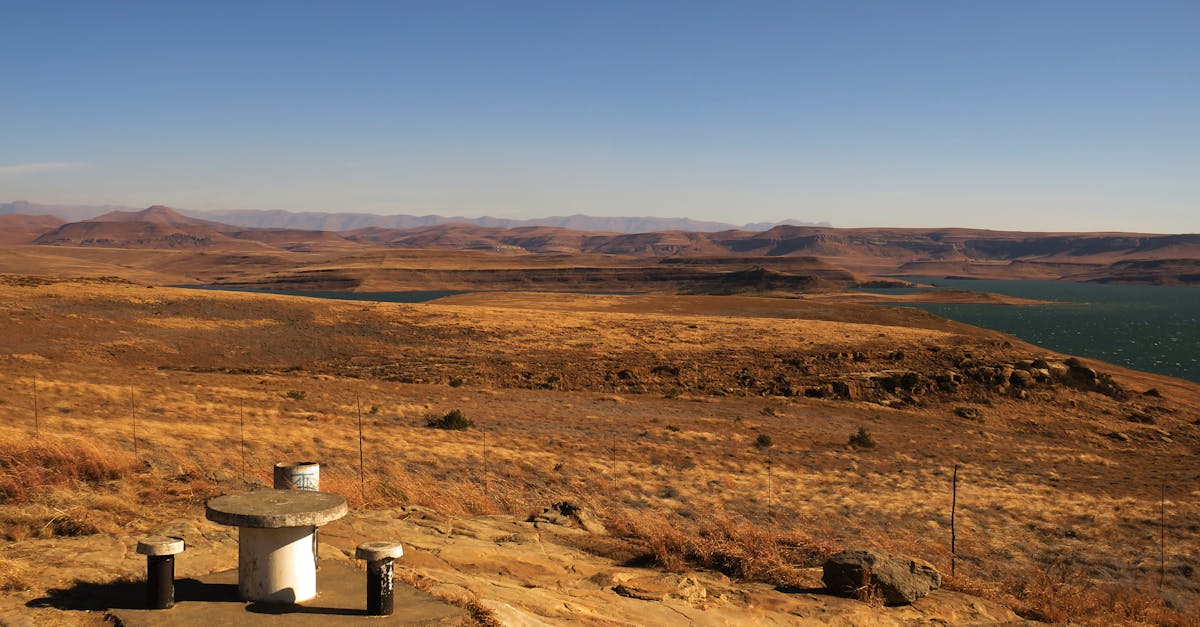 Panoramic view of a vast, arid landscape with a dam and a distant mountain range under a clear sky.