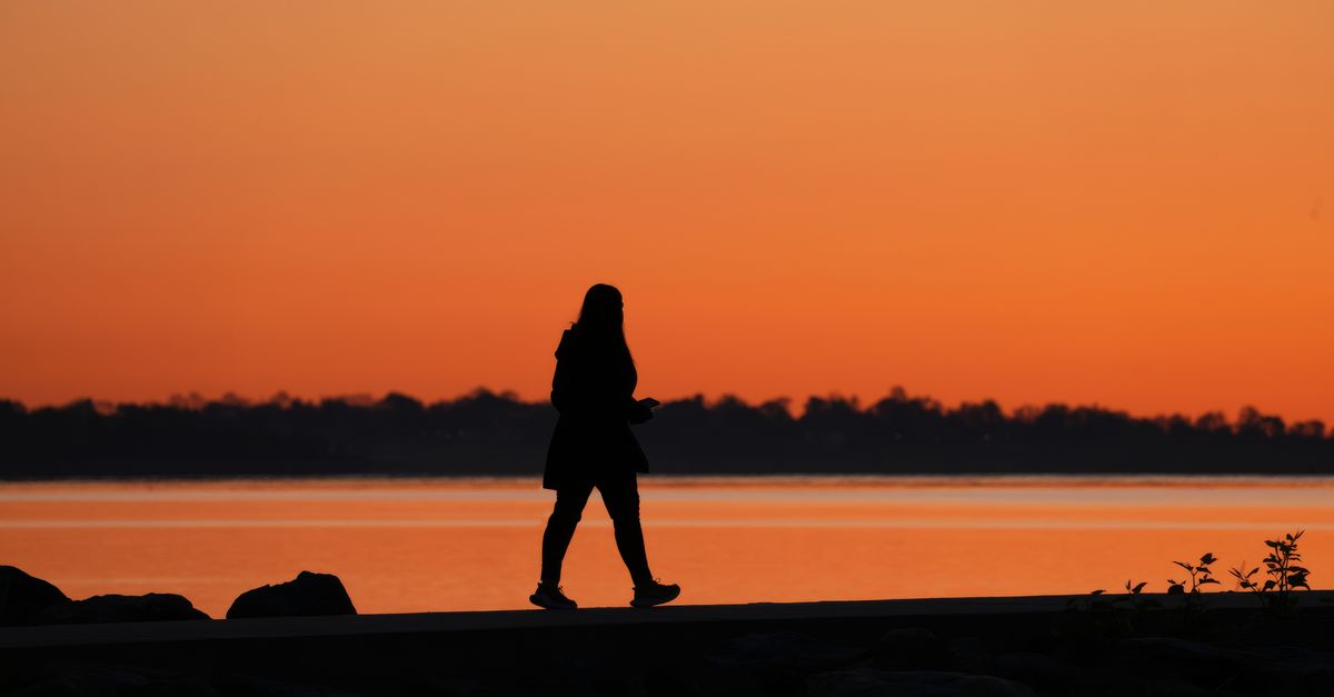A serene silhouette of a woman strolling by a lake during a vibrant sunset.