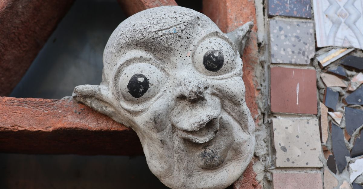 A whimsical gargoyle sculpture decorates an artistic urban wall, surrounded by mosaic tiles.