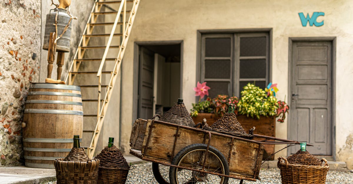 Vintage courtyard featuring a wooden cart, wicker baskets, and barrels against a rustic building.