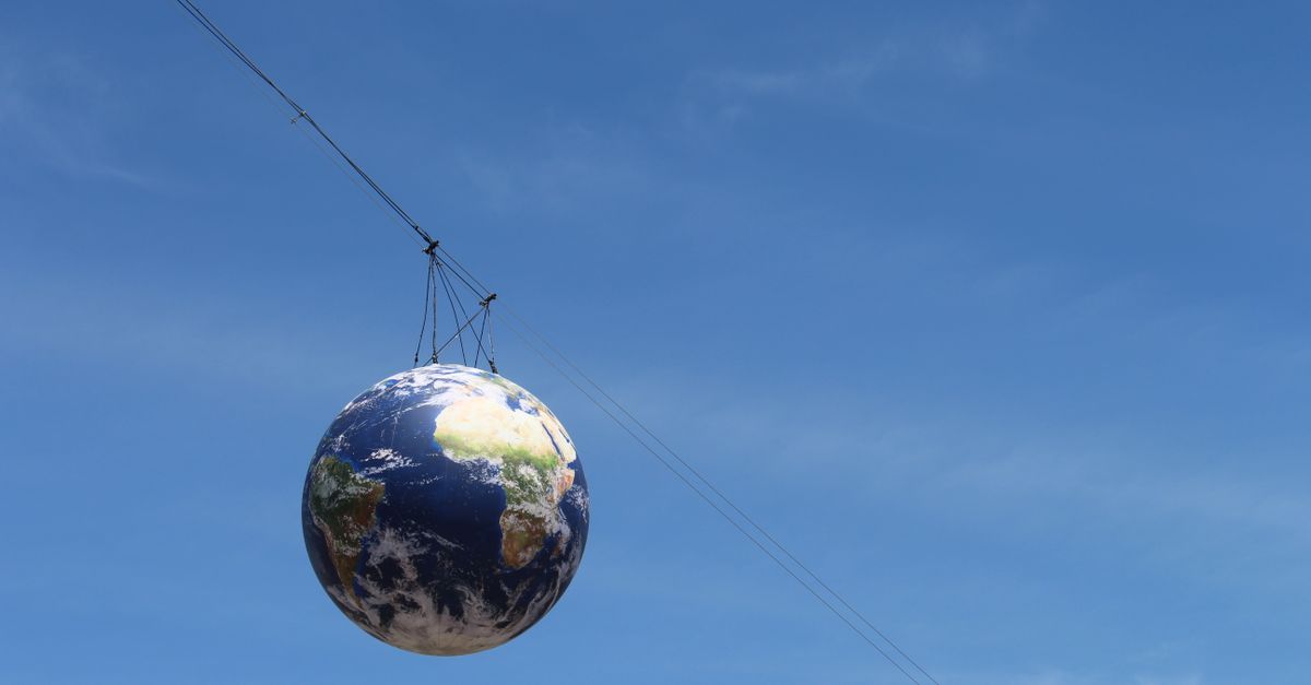 A realistic globe hanging on cables against a vivid blue sky, representing global unity.