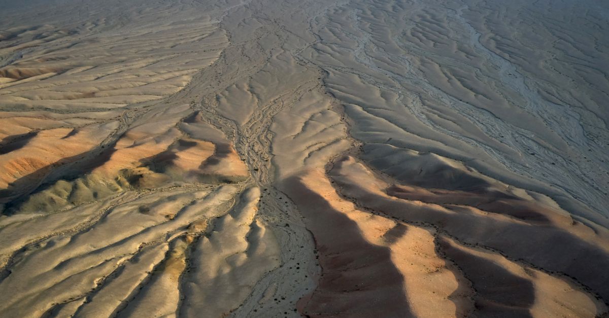 From above of dry terrain with arid soil covered with sand forming wavy lines on surface in daylight