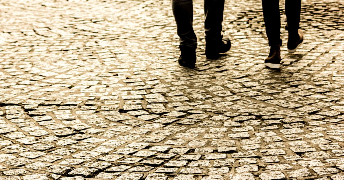 Two people walking on a textured cobblestone street, capturing motion and pattern.