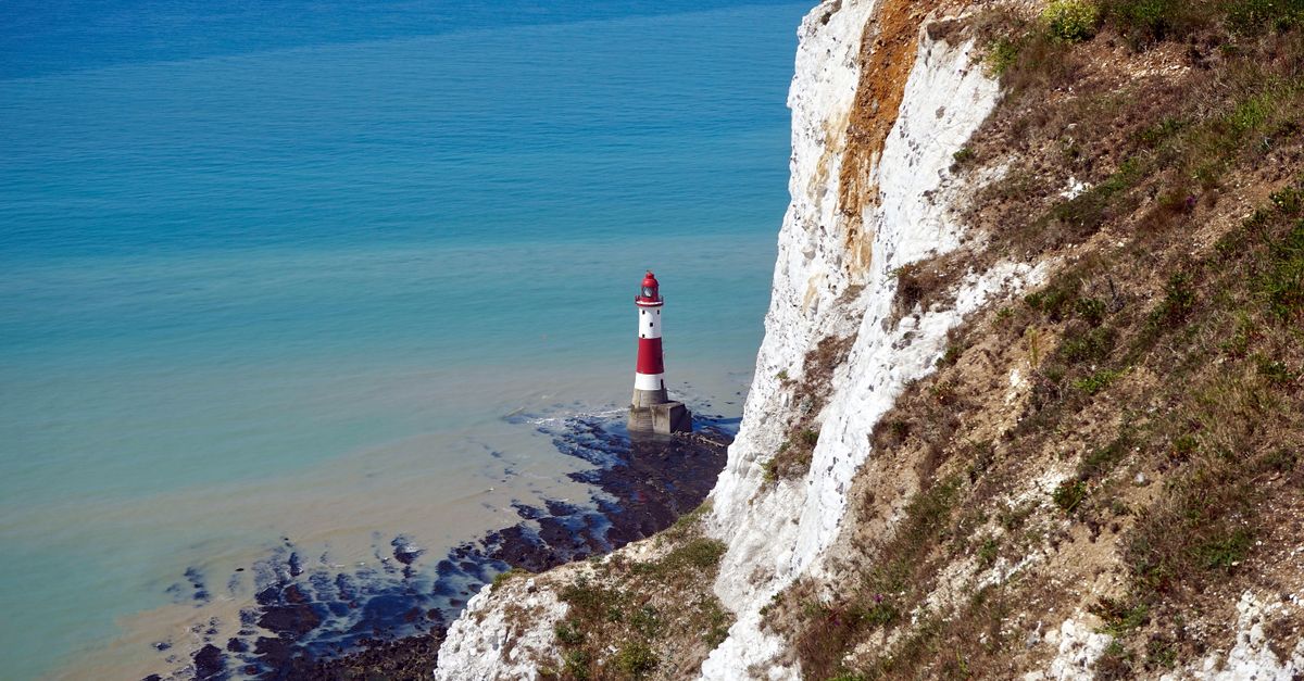Stunning view of Beachy Head Lighthouse nestled beside the iconic white chalk cliffs and calm sea.