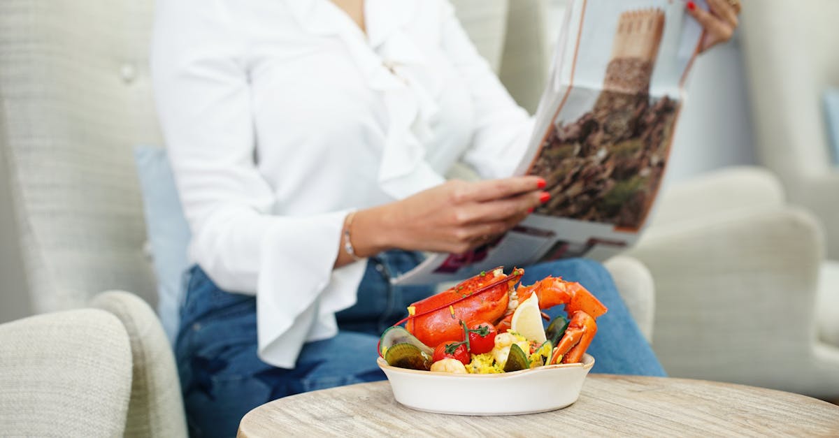 A woman enjoys a seafood dish in a cozy indoor setting while reading a newspaper.