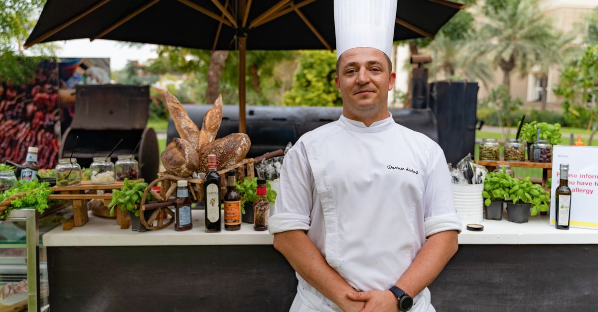 Chef in a white uniform and hat standing in an outdoor restaurant setting in Dubai.