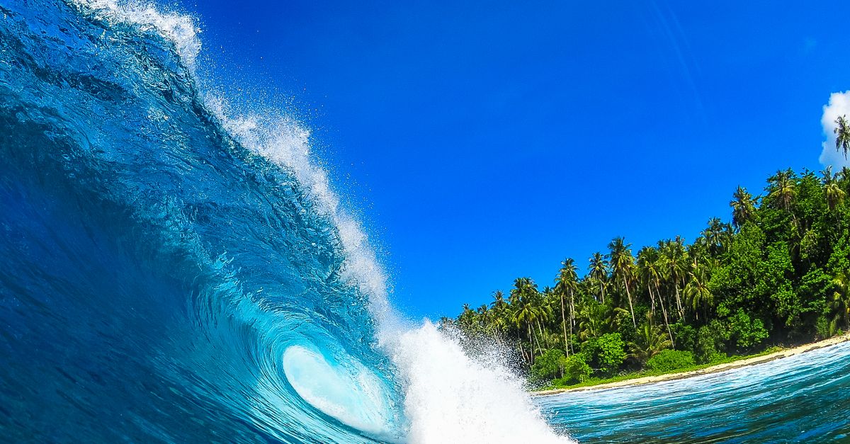 Vivid capture of a wave crashing against a tropical beach under a clear blue sky.