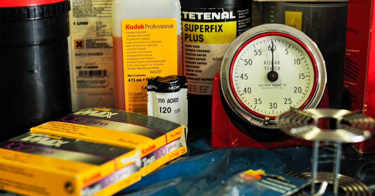 Collection of analog photography items including film rolls, developer liquids, and a Kodak timer for darkroom processing.