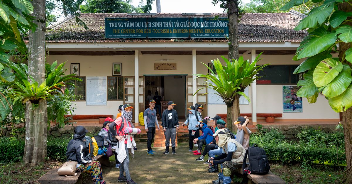 Group of travelers with backpacks for hiking sitting near tourist agency in tropical lush forest