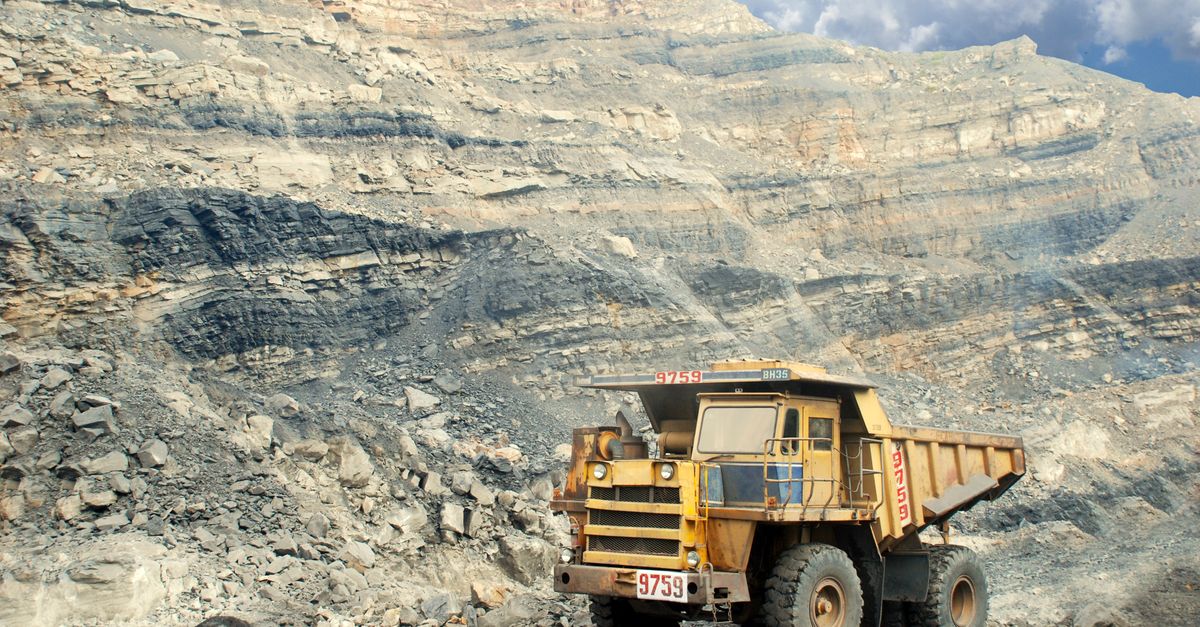 A large yellow mining truck in a rocky quarry under a clear sky.