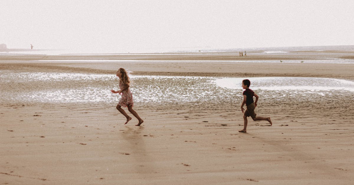 Full body of barefoot children running along seashore near water against cloudless sky in summer day during vacation in tropical country