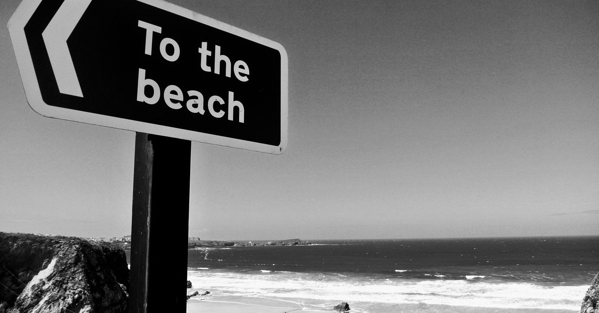 Black and white photo of a 'To the Beach' sign with stunning ocean view at Cornwall, UK.