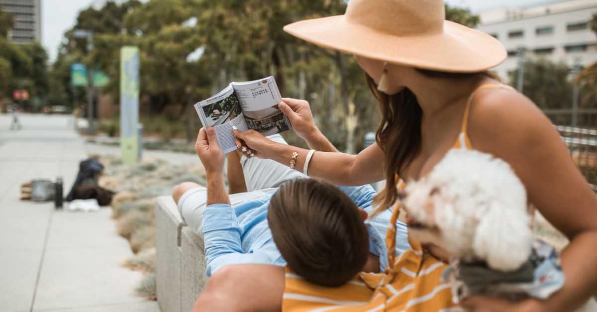 A couple enjoys a relaxing day outdoors, reading a book with their pet dog close by.