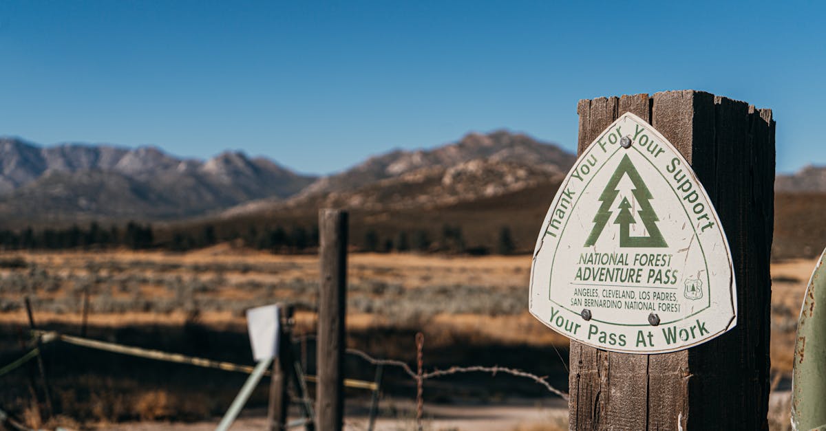 Close-up of National Forest Adventure Pass sign on wooden post with mountains in the background.