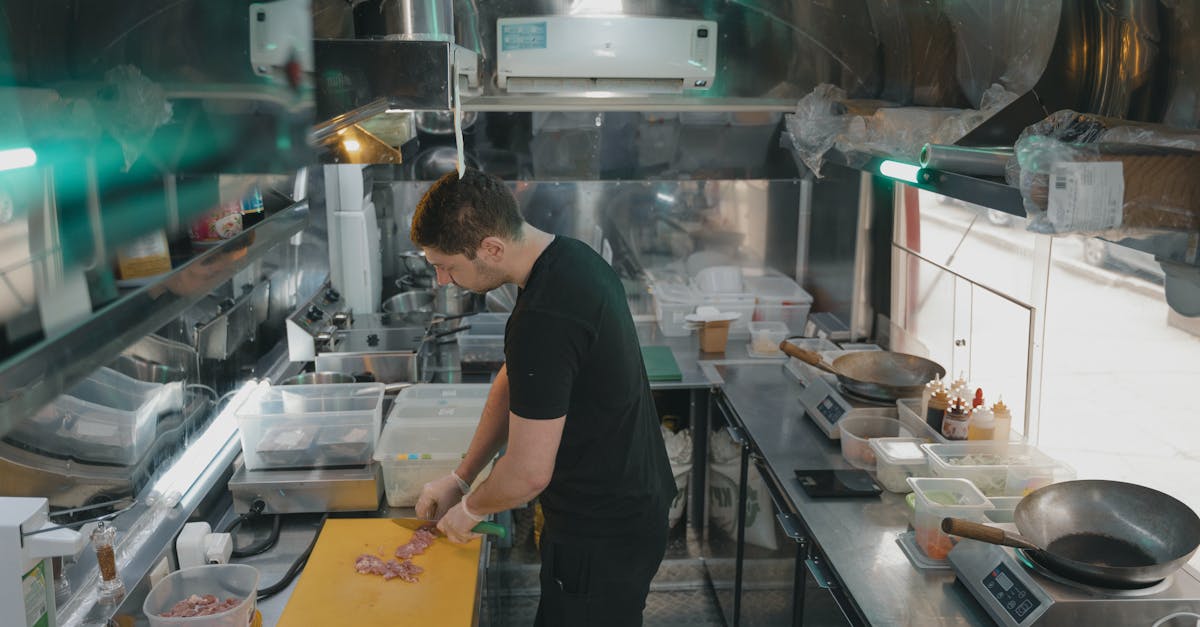 A chef works in a modern industrial kitchen, slicing ingredients on a yellow cutting board.
