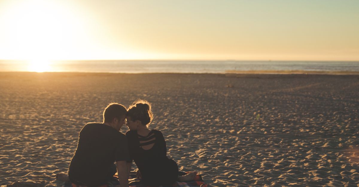 A couple enjoys sunset together on a sandy beach, capturing a moment of love and togetherness.