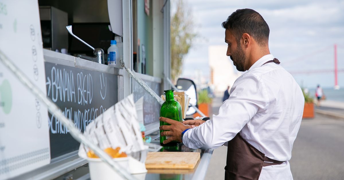 Side view of ethnic male cook in uniform arranging food and bottles on counter of food truck